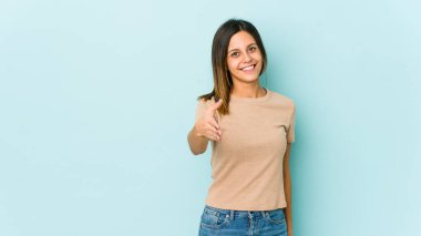 Mavi arka planda izole edilmiş genç bir kadın selamlama jesti olarak kameraya uzanıyor..