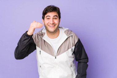 Mor arka planda izole olmuş genç bir adam bir şeye gülüyor, elleriyle ağzını kapatıyor..