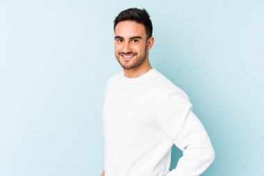 Kafkasyalı genç, mavi arka planda izole edilmiş. Kendine güvenen, kalçaları tutan biri..