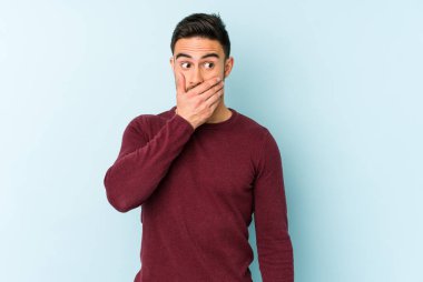 Kafkasyalı genç adam mavi arka planda izole edilmiş. Düşünceli bir şekilde ağzıyla ağzını kapatan bir fotokopi odasına bakıyor..