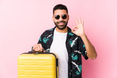 Elinde neşeli ve kendinden emin bir bavul tutan genç latin adam iyi bir jest yapıyor..