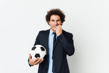Futbol antrenörü elinde bir topla tırnak yiyor. Gergin ve endişeli..