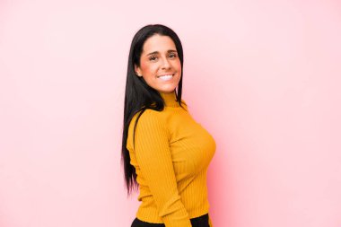 Pembe arka planda soyutlanmış genç beyaz kadın gülümseyen, neşeli ve keyifli bir kenara bakıyor..