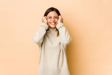 Bej arka planda izole edilmiş genç bir kadın kulakları elleriyle kapatıyor..