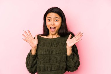 Pembe arka planda yalnız yaşayan genç Çinli kadın zaferi ya da başarıyı kutluyor, şaşırıyor ve şok oluyor..