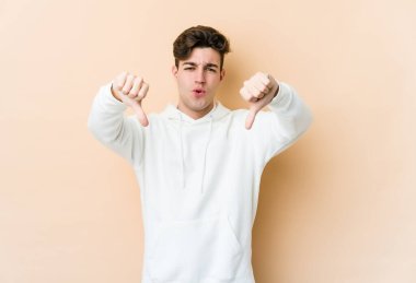 Beyazların arka planında izole edilmiş genç beyaz bir adam baş parmağını aşağı gösteriyor ve hoşlanmadığını ifade ediyor..