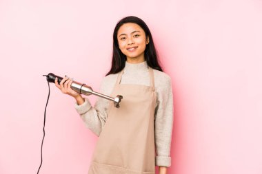 Elinde mikser tutan genç Çinli bir kadın gömlek fotokopisini elle işaret ediyor, gururlu ve kendinden emin.