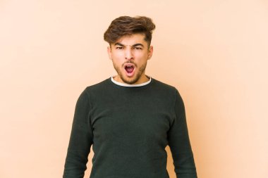 Genç Arap bir adam bej bir arka planda izole edilmiş çok kızgın ve agresif çığlık atıyor..