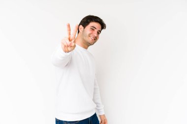 Beyaz arka planda izole edilmiş genç adam neşeli ve kaygısız parmakları olan bir barış sembolü gösteriyor..
