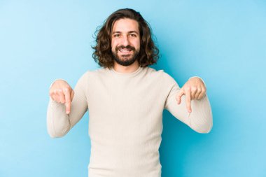 Genç, uzun saçlı adam mavi arka planda izole edilmiş. Parmakları aşağıda. Olumlu bir his..