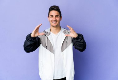 Mor arka planda izole edilmiş genç beyaz bir adam elinde avuç içi bir şeyle kameraya sunuyor..