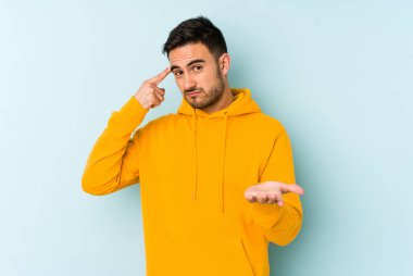 Kafkasyalı genç adam mavi arka planda izole edilmiş ve elinde bir ürün tutuyor..