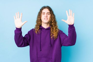 Uzun saçlı adam yalnız poz veriyor. 10 numarayı elleriyle gösteriyor..