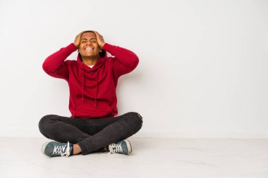 Yerde tek başına oturan genç latin adam mutlu bir şekilde ellerini başının üstünde tutarak gülüyor. Mutluluk kavramı.