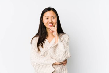 Genç Çinli kadın kendini izole edip gülümsüyor mutlu ve kendinden emin, elleriyle çenesine dokunuyor..