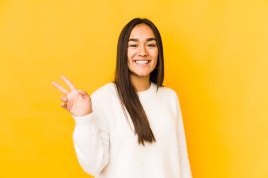 Sarı arka planda izole edilmiş genç bir kadın neşeli ve kaygısız parmakları olan bir barış sembolü gösteriyor..