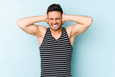 Kafkasyalı genç adam mavi arka planda izole edilmiş kulakları kulaklarıyla kapatıyor çok fazla ses duymamaya çalışıyor..