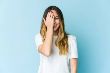 Mavi arka planda izole edilmiş genç beyaz kadın yüzünün yarısını palmiyeyle kaplarken eğleniyor..
