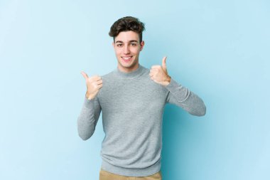 Young caucasian man isolated on blue background raising both thumbs up, smiling and confident. clipart