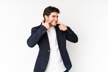 Beyaz arka planda izole edilmiş genç iş adamı gülümsüyor, parmaklarını ağıza doğrultuyor..