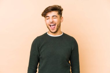 Genç Arap bir adam bej bir arka planda izole edilmiş komik ve dost canlısı bir dil kullanıyor..