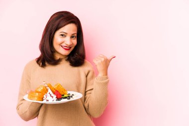 Orta yaşlı Latin bir kadın elinde waffle tutarken izole edilmiş gülümsüyor ve başparmağını kaldırıyor.
