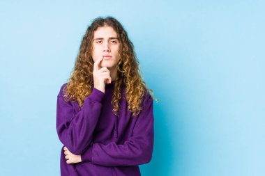 Uzun saçlı adam şüpheli ve şüpheci ifadesiyle yanlamasına poz veriyor..