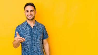 Sarı fırında izole edilmiş genç beyaz adam kameraya elini uzatarak selam veriyor..