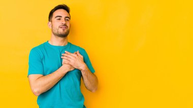 Sarı fırında izole edilmiş beyaz bir genç, dost bir ifadeye sahip, avuçlarını göğsüne bastırıyor. Aşk konsepti.