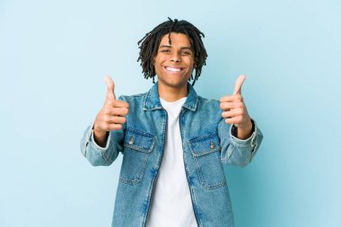 Kot ceket giyen genç siyah adam gülümsüyor ve başparmağını kaldırıyor.