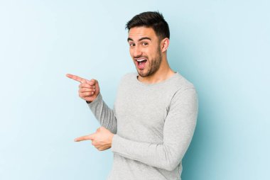 Mavi arka planda izole edilmiş genç beyaz adam işaret parmağıyla fotokopi alanını işaret ederek heyecan ve arzusunu ifade ediyor..