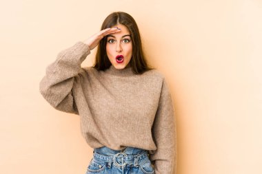 Beyazlı genç bir kadın bej arka planda izole edilmiş, uzaklara bakıyor ve elini alnına koyuyor..