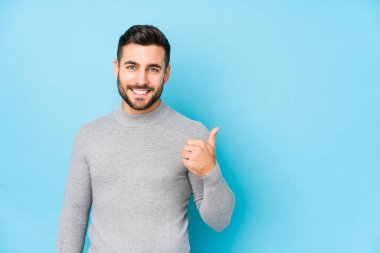 Mavi arka planda genç beyaz bir adam izole edilmiş gülümsüyor ve başparmağını kaldırıyor.