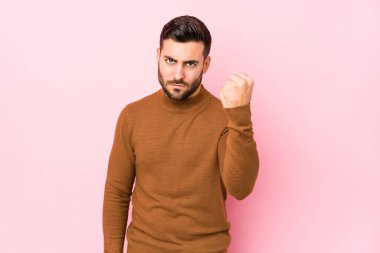 Pembe arka planda genç beyaz bir adam izole edilmiş, yumruğunu kameraya gösteriyor, agresif yüz ifadesi var..