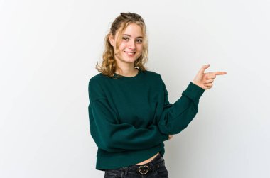 Beyaz arka planda genç beyaz kadın işaret parmağıyla işaret ederek gülümsüyor..