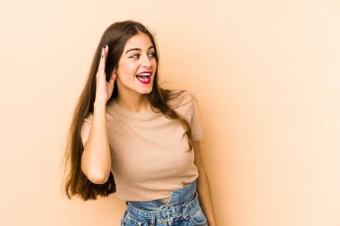 Beyazlı genç bir kadın bej arka planda izole edilmiş bir şekilde bir dedikoduyu dinlemeye çalışıyor..