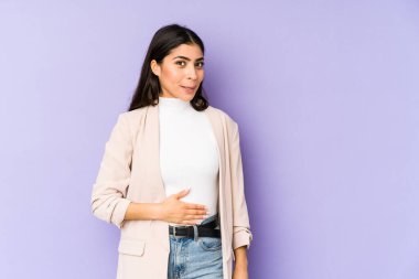 Mor arka planda izole edilmiş genç Hintli kadın karnına dokunur, nazikçe gülümser, yemek yer ve tatmin olur..