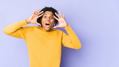 Rasta saç stili giyen genç siyah adam hoş bir sürpriz yapıyor, heyecanlı ve el kaldırıyor..