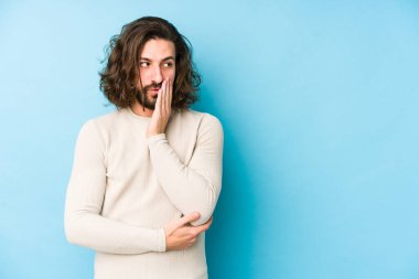 Mavi arka planda izole edilmiş uzun saçlı genç adam gizli bir sıcak fren haberi veriyor ve yana bakıyor.