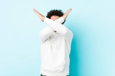 Mavi arka planda genç sporcu iki kolu çapraz tutuyor, inkar kavramı.