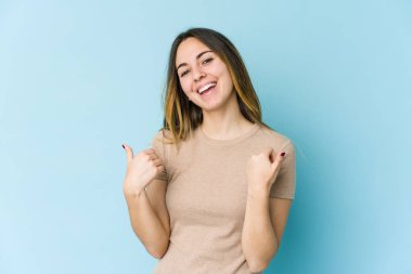 Kafkasyalı genç bir kadın mavi arka planda izole edilmiş. Baş parmağını kaldırıyor, gülümsüyor ve kendinden emin..