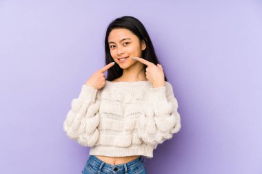 Mor arka planda izole edilmiş genç Çinli kadın gülümsüyor, parmaklarını ağıza doğrultuyor..
