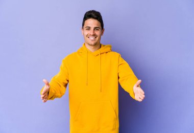 Mor arka planda izole genç beyaz adam iki eliyle bir şey tutuyor, ürün sunumu..