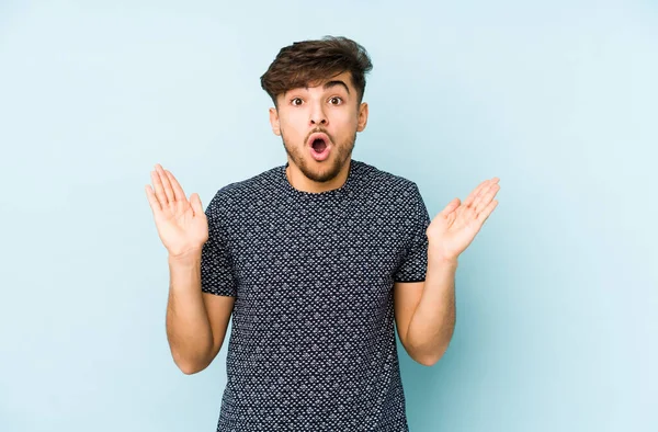 Mavi arka planda yaşayan genç Arap adam şaşırdı ve şok oldu..