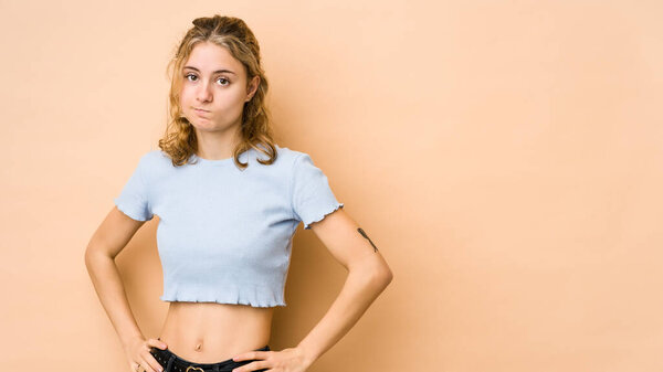 Молодая кавказская женщина, изолированная на бежевом фоне, смущена, чувствует сомнение и неуверенность.