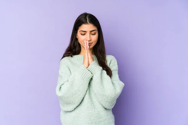 口の近くで祈る手を握って紫色の背景に隔離された若いインド人女性は 自信を感じています — ストック写真