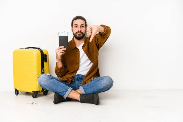 パスポートを持って座っている若い白人男性と 嫌なジェスチャー 親指を下に示すスーツケースが隔離されています 意見の相違 — ストック写真