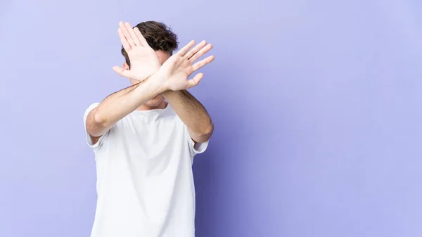 stock image Young caucasian man isolated on purple background keeping two arms crossed, denial concept.