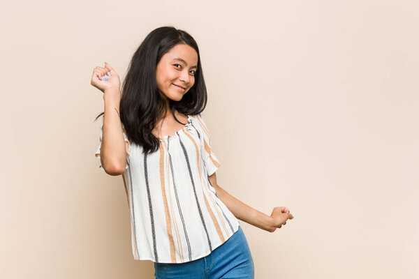 Молодой милый китайский подросток Молодая блондинка в пальто на розовом фоне танцует и весело.