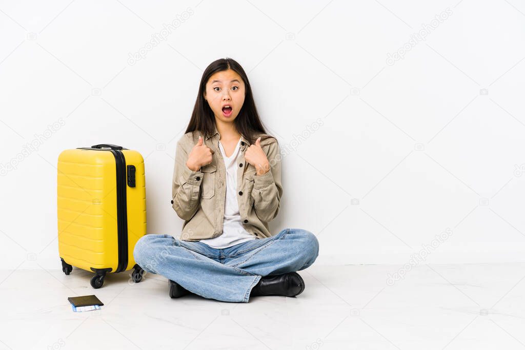 Young chinese traveler woman sitting holding a boarding passes surprised pointing with finger, smiling broadly.